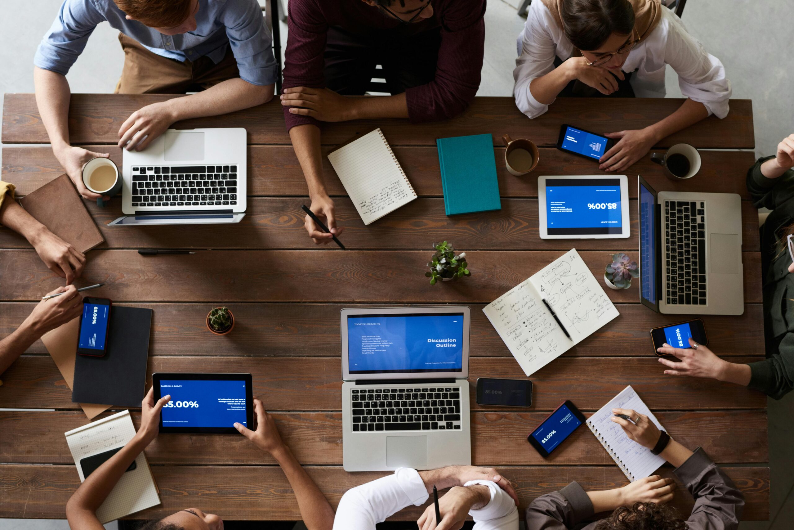 Team of professionals collaborating on laptops and digital devices around a wooden table.